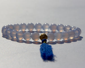 The Healers bracelet, blue chalcedony.  With a 24k gold bead and blue cotton tassel.  Blue chalcedony helps create the Sacred voice. It also has strong color healing abilities.  Stretch bracelet. Length: 18 cms.