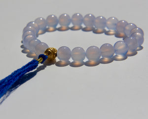 The Healers bracelet, blue chalcedony.  With a 24k gold bead and blue cotton tassel.  Blue chalcedony helps create the Sacred voice. It also has strong color healing abilities.  Stretch bracelet. Length: 18 cms.