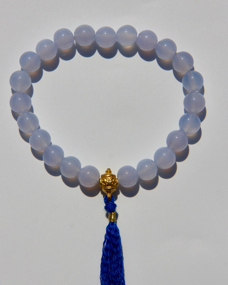 The Healers bracelet, blue chalcedony.  With a 24k gold bead and blue cotton tassel.  Blue chalcedony helps create the Sacred voice. It also has strong color healing abilities.  Stretch bracelet. Length: 18 cms.