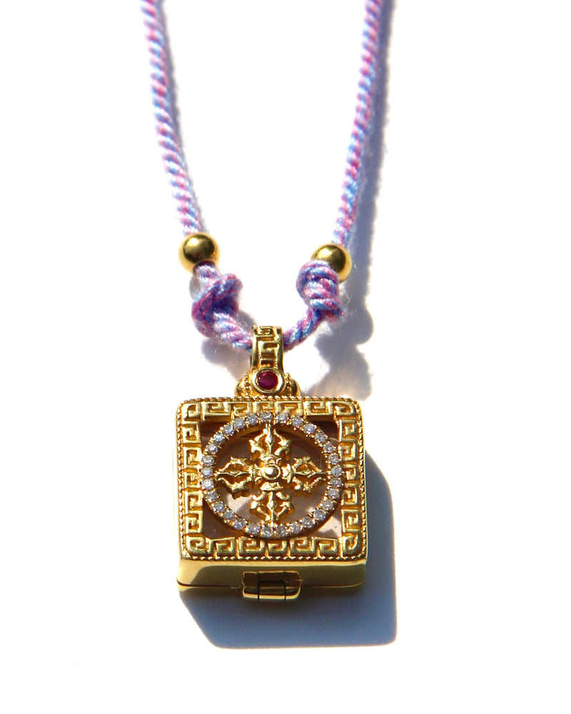 Miniature Treasure box, with a double vajra / dorje made of 18k gold, white diamonds and one pink sapphire.  Knotted cotton thread.  Two 24k gold beads.  Sold with Magical dusts to fill the miniature box.